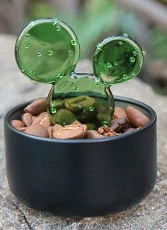 a mickey mouse figurine sitting in a black container filled with rocks and pebbles