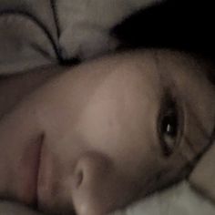 a close up of a person laying in bed with their head on the pillow and looking at the camera