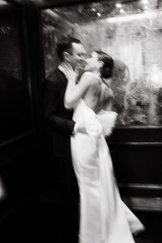 black and white photograph of a bride and groom kissing in front of a store window