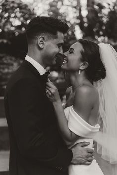 black and white photo of bride and groom smiling at each other with trees in the background