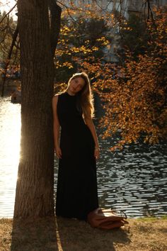 a woman standing next to a tree in front of a lake