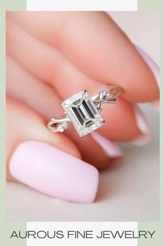 a woman's hand holding a ring with an emerald stone in the middle and a white manicured nail