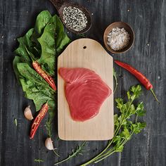 raw fish on a cutting board surrounded by greens and spices