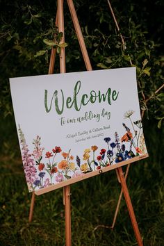 a welcome sign sitting on top of a easel in front of some grass and trees