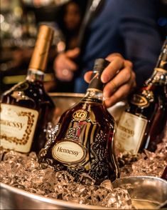 three bottles of henessy are sitting on ice in a bowl with silver spoons