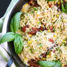 a skillet filled with pasta and vegetables on top of a striped towel next to a fork