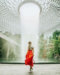 a woman in a red skirt is walking through an indoor area with a fountain behind her