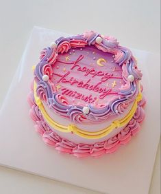 a birthday cake with pink and purple frosting on top of a white tablecloth