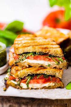 two grilled sandwiches stacked on top of each other with pesto and tomatoes in the background