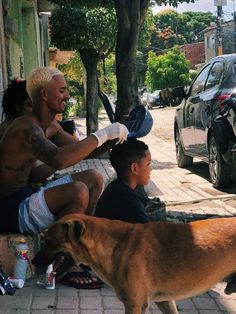 two men are sitting on the sidewalk with a dog and another man is standing next to them