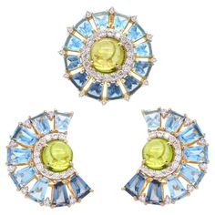 18k gold blue topaz tapered baguette peridot cabochon pendant earrings set Elevate your jewelry collection with our exquisite 18K gold blue topaz peridot ferris wheel pendant earrings set, a stunning piece that showcases the perfect blend of vibrant colors and intricate design. At the heart of the set, lies a mesmerising peridot cabochon, radiating its unique yellowish green glow. Encircling the peridot is a halo of sparkling diamonds, meticulously set to enhance its luminous beauty. The outer layer features a dazzling array of prong-set London blue topaz, Swiss blue topaz and sky blue topaz gemstones, each one selected for its exceptional clarity and vivid blue hue from dark to light. These gemstones are arranged in a captivating ferris wheel pattern, creating a beautiful contrast with th