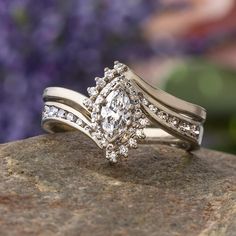 two wedding rings on top of a rock with purple flowers in the background