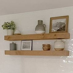 two wooden shelves with pictures and vases on them in a white tiled bathroom area