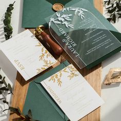 the wedding stationery is laid out on top of green envelopes and gold foil