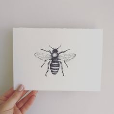 a hand holding up a piece of paper with a drawing of a bee on it