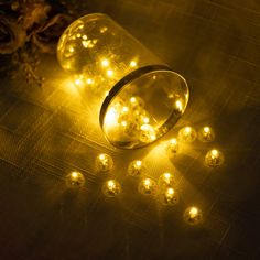 a glass jar filled with yellow lights sitting on top of a table next to flowers