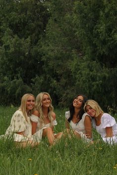 three beautiful women sitting in the grass with trees in the backgroung behind them