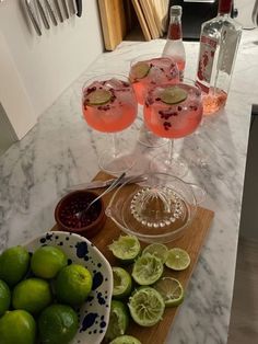 three glasses filled with pink wine and limes on a marble counter top next to bowls of fruit