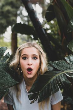 a woman with her mouth open standing in front of some green plants and palm leaves