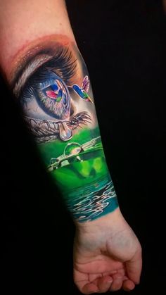 an eye tattoo on the left arm with water and green grass in front of it