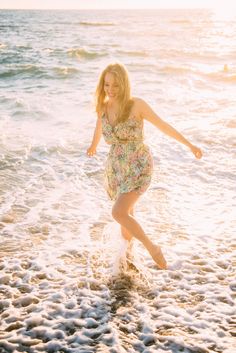 a woman in a floral dress is running through the water at the beach on a sunny day