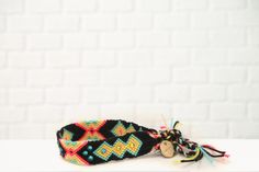 a black bracelet with colorful beads and tassels sitting on top of a white table