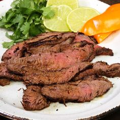 a white plate topped with meat and veggies next to a slice of lime