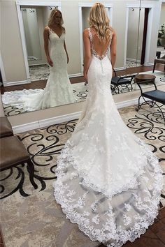 a woman standing in front of a mirror wearing a wedding dress with an open back