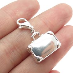 a hand holding a silver charm with a small square shaped object on it's side