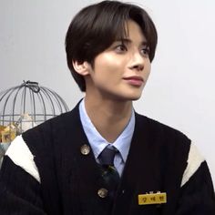 a young man wearing a sweater and tie in front of a cage with birds on it