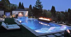 an outdoor pool at night with lounge chairs and fire pit in the backgroud