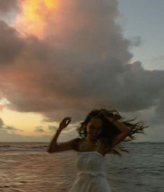 a woman in a white dress is standing on the beach with her hair blowing in the wind