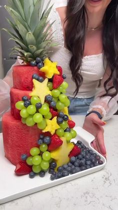 a woman standing in front of a cake made to look like a pineapple and grapes