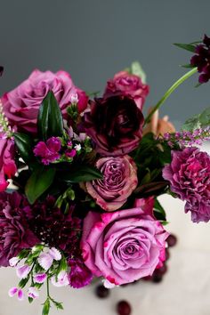 a vase filled with purple flowers on top of a white countertop next to berries and greenery