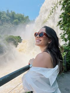 a woman wearing sunglasses standing in front of a waterfall