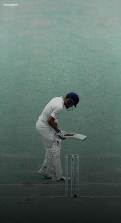 a man in white is playing cricket on the grass and water behind him, holding a bat