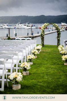 a row of white chairs sitting on top of a lush green field next to a body of water