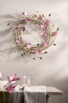 a wreath with pink flowers hanging from the side of a wall next to a table