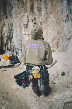 a man climbing up the side of a mountain with backpacks on his back and other items around him