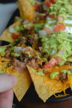 someone is holding up some nachos with meat, cheese and guacamole