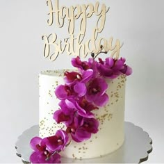 a white cake with purple flowers on top and the words happy birthday written in gold