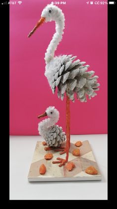 a bird made out of pine cones is standing next to a baby bird on a checkered board