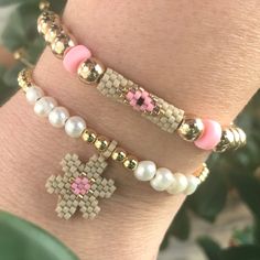 two bracelets with cross charms and beads on the wrist, one is pink and white