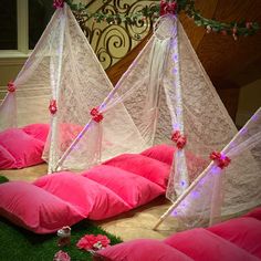 some pink pillows are on the ground with white netting over them and flowers around them