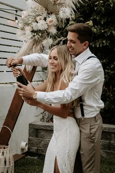 a man and woman standing next to each other in front of a wooden structure with flowers on it