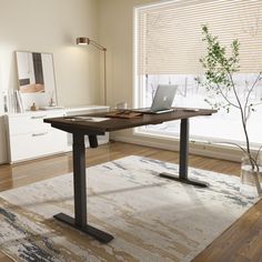 a desk with a laptop on it in front of a window and a potted plant