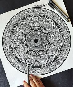 a person is drawing a black and white design on paper