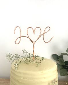 a white cake topped with a metal love sign and greenery on top of a wooden table