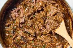 a pot full of beef and gravy with a wooden spoon