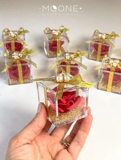 someone is holding a small glass box with roses in it and gold ribbon on the top